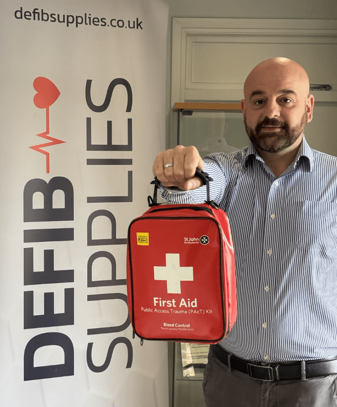 Screenshot 2025-06-17 095611 Defib Supplies team member holding a St John Ambulance bleed control kit in front of company banner